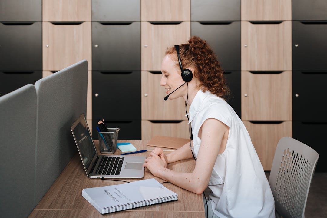 Woman wearing headset working at a laptop in a modern office environment. Ideal for telecommuting themes.